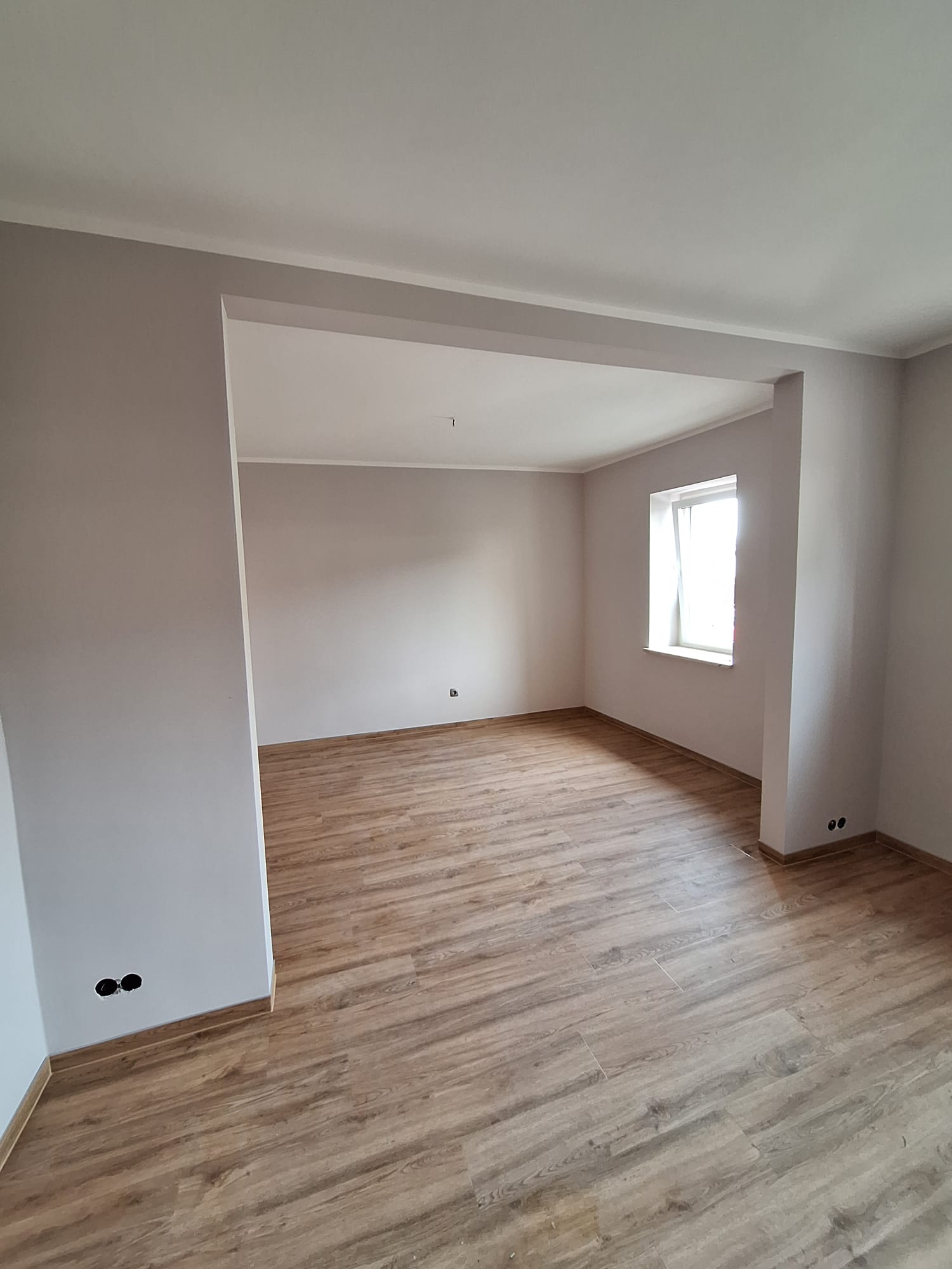 Renovierter Wohnraum mit frisch gestrichenen Wänden und neu verlegtem Boden in Holzoptik